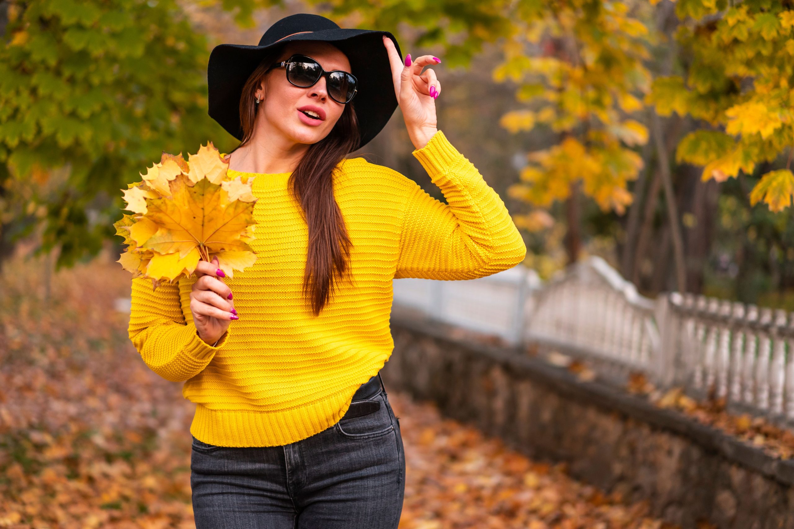 Femme en tenue chic d'automne tenant des feuilles jaunes