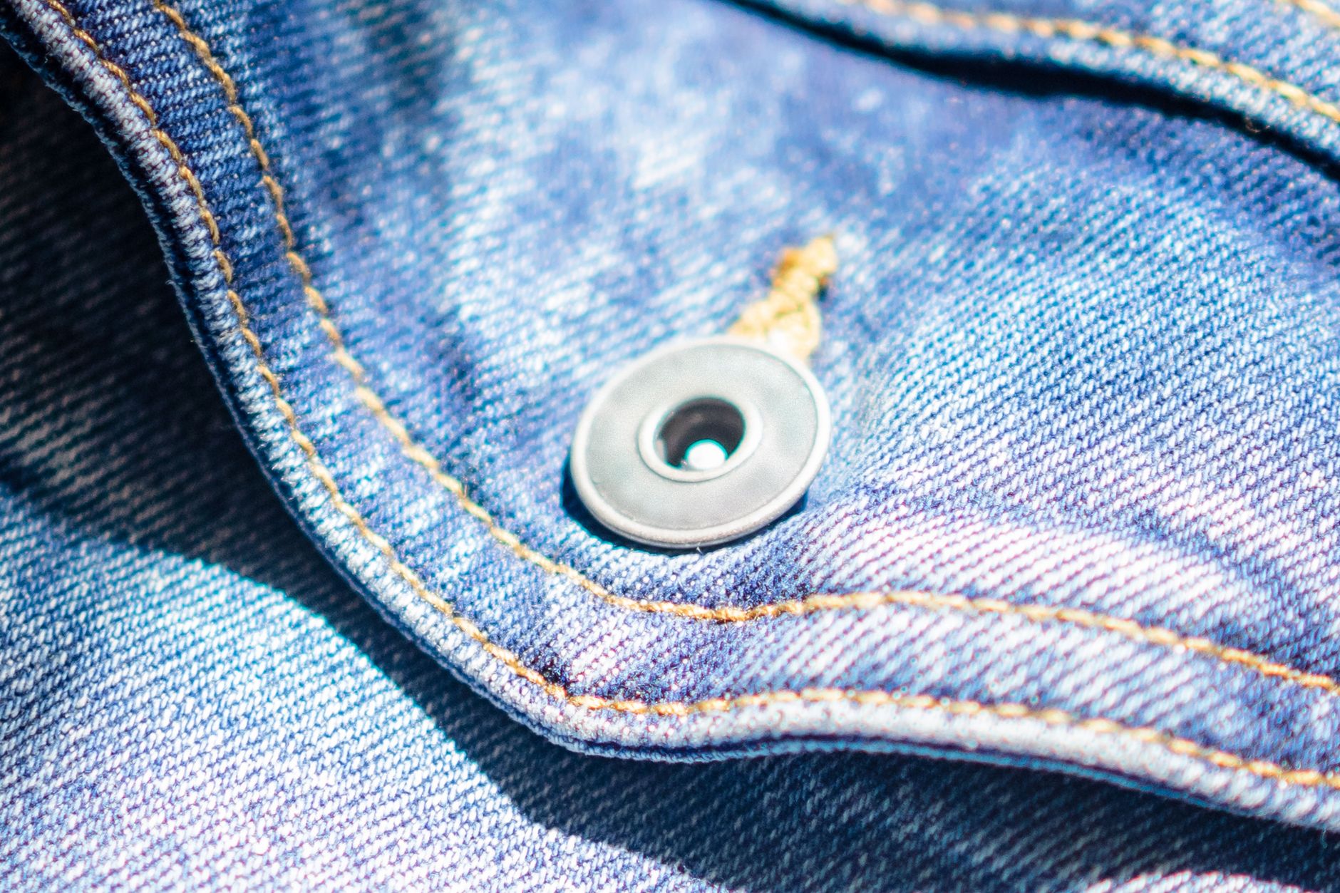 Gros plan sur le boutonnage métal et les surpiqûres contrastées d'une toile de denim