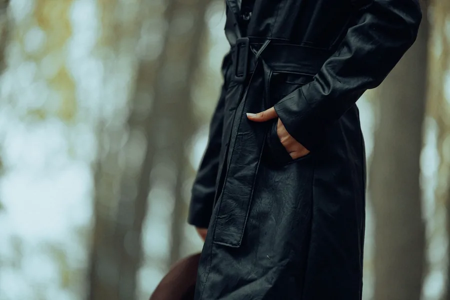 Poche d'un manteau long sombre, main posée, dans un sous-bois d'automne