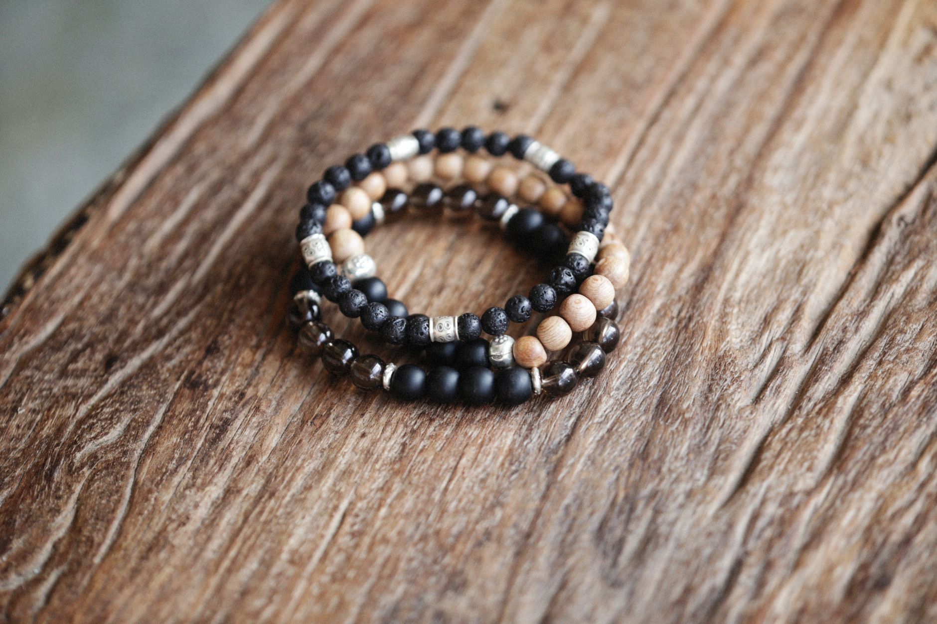 trois bracelets de perles rondes, pierre noire et bois clair, posés sur une table en bois