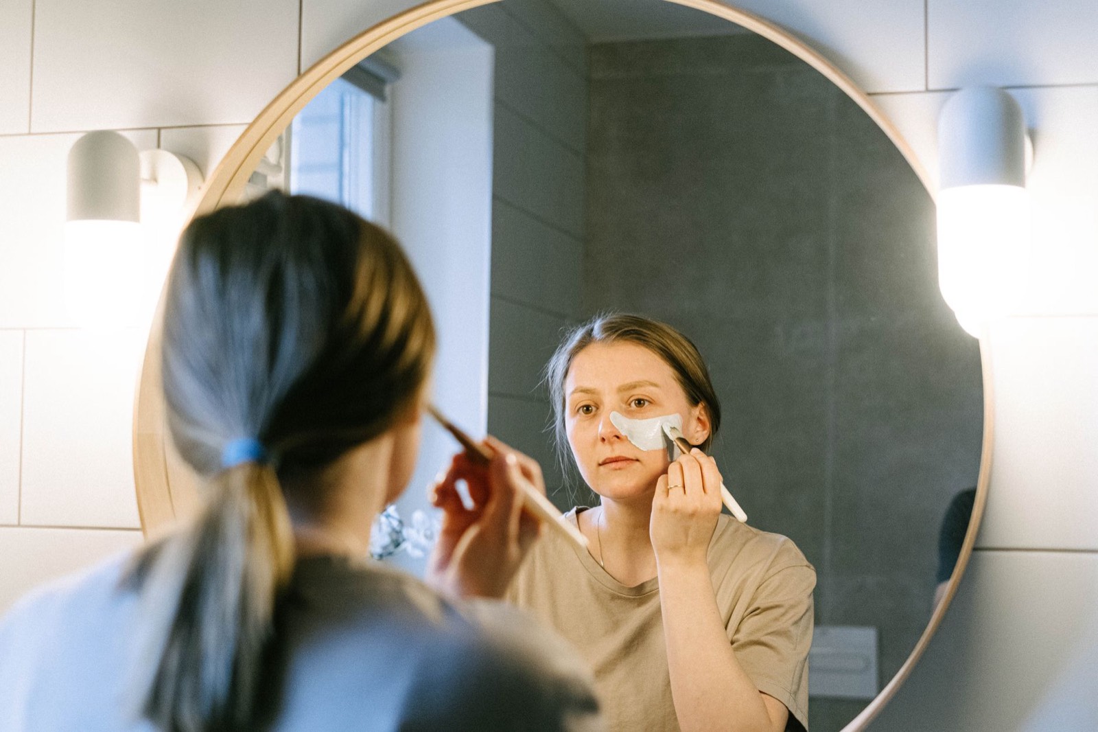 Femme appliquant une crème solaire sur son visage devant un miroir de salle de bain